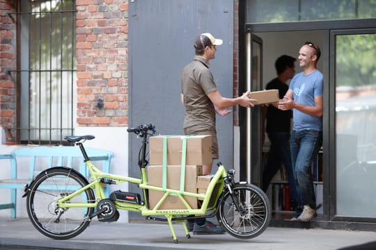 Paketbote mit Lastenrad bei der Auslieferung eines Pakets